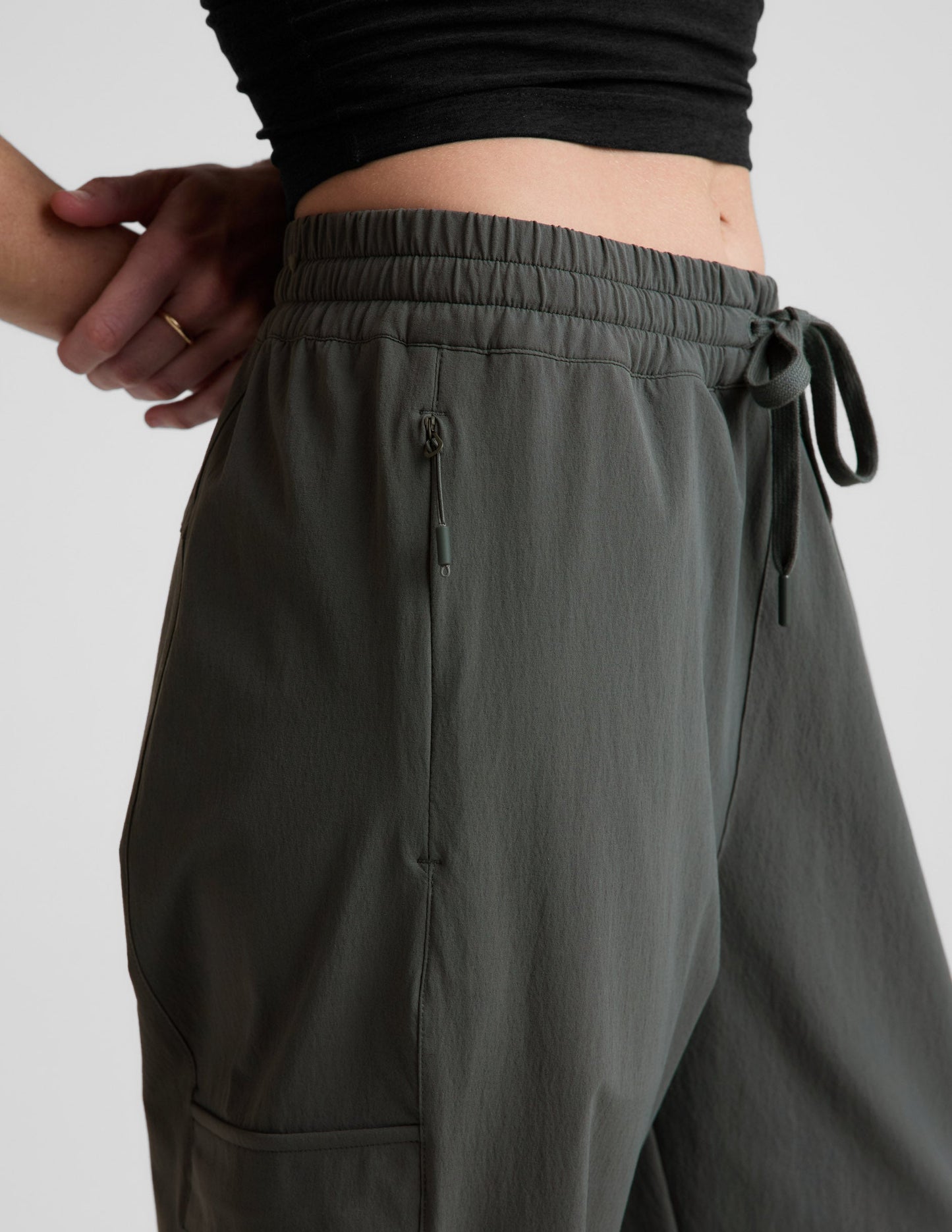 Woman wearing Java Peak Pant with a black cropped top, featuring a close-up of the elastic waistband and zipper pocket.