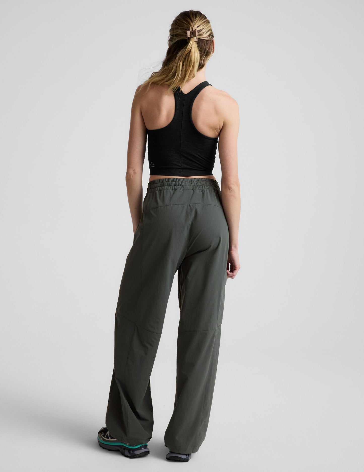 Rear view of woman wearing dark olive Peak Pant™ with a gathered waistband, paired with a black racerback tank top.