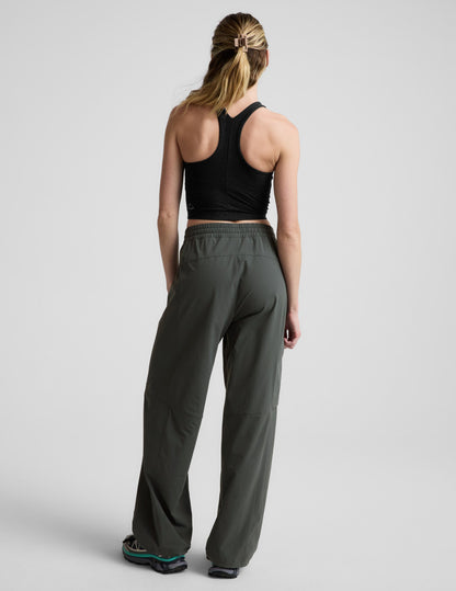 Rear view of woman wearing dark olive Peak Pant™ with a gathered waistband, paired with a black racerback tank top.