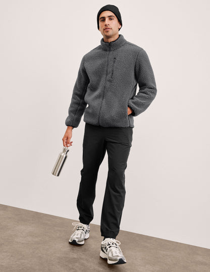 Man in navy On The Go Men's Jogger with cuffed ankles, grey fleece jacket, and beanie, holding a silver water bottle.