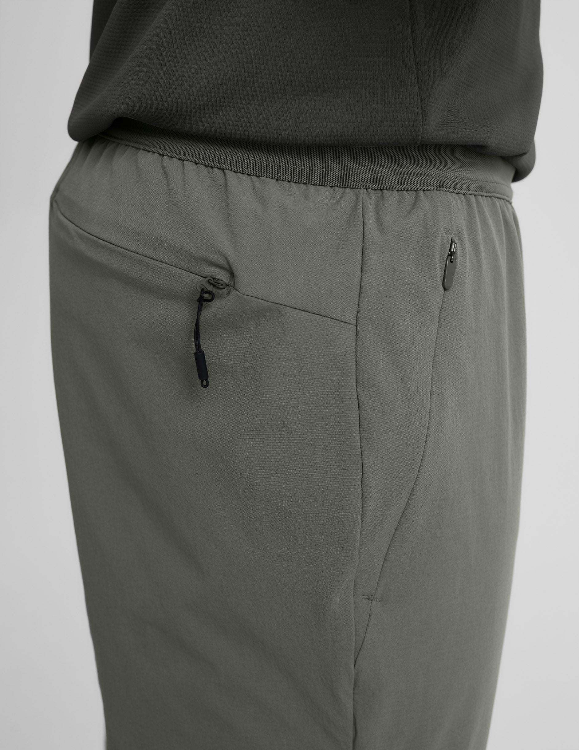 Side view of olive On The Go Men's Jogger highlighting the elastic waistband and discrete side and back zipper pockets.