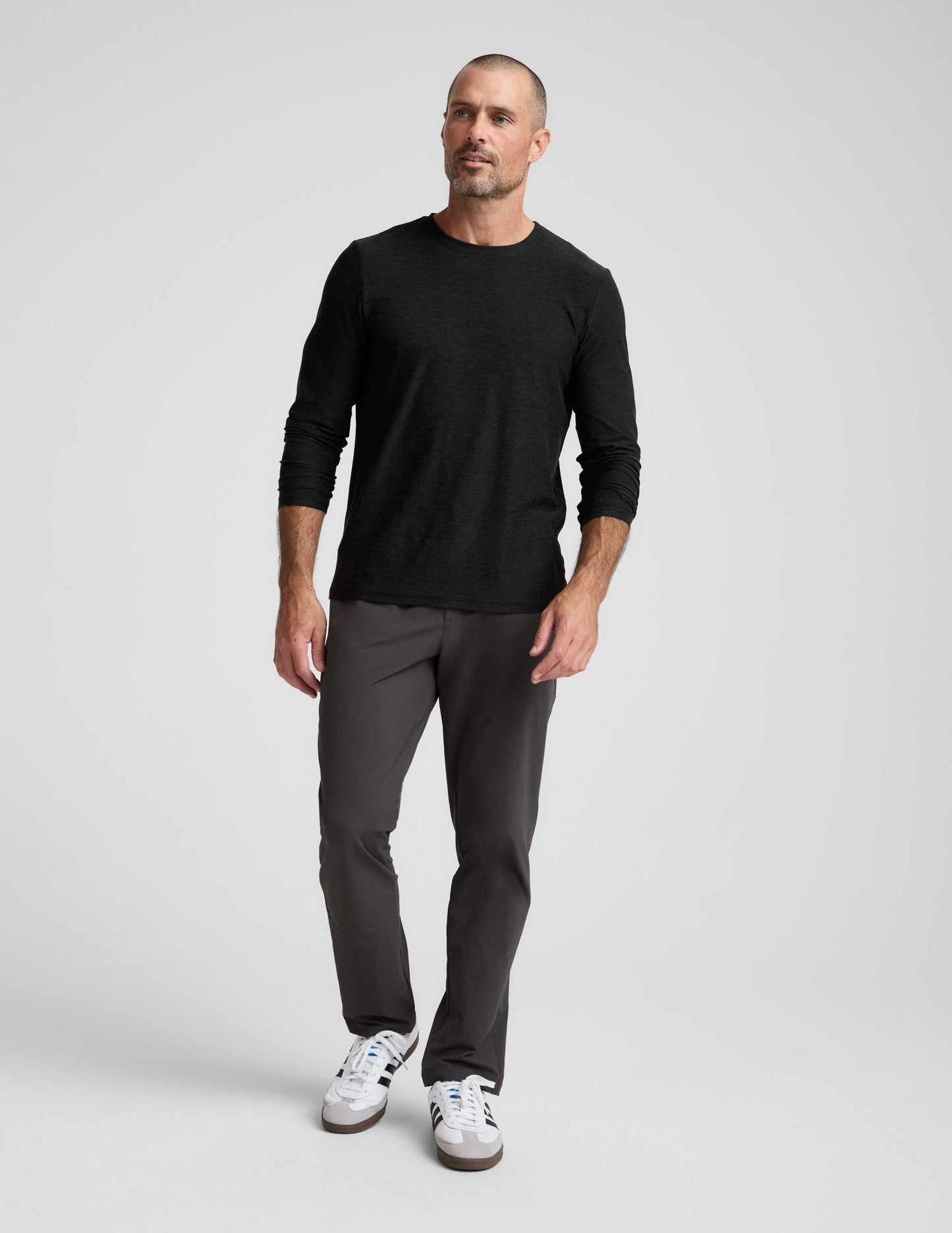 Man walking in dark charcoal Men's All Terrain Pant with a straight-leg fit, black long-sleeve shirt, and white sneakers.