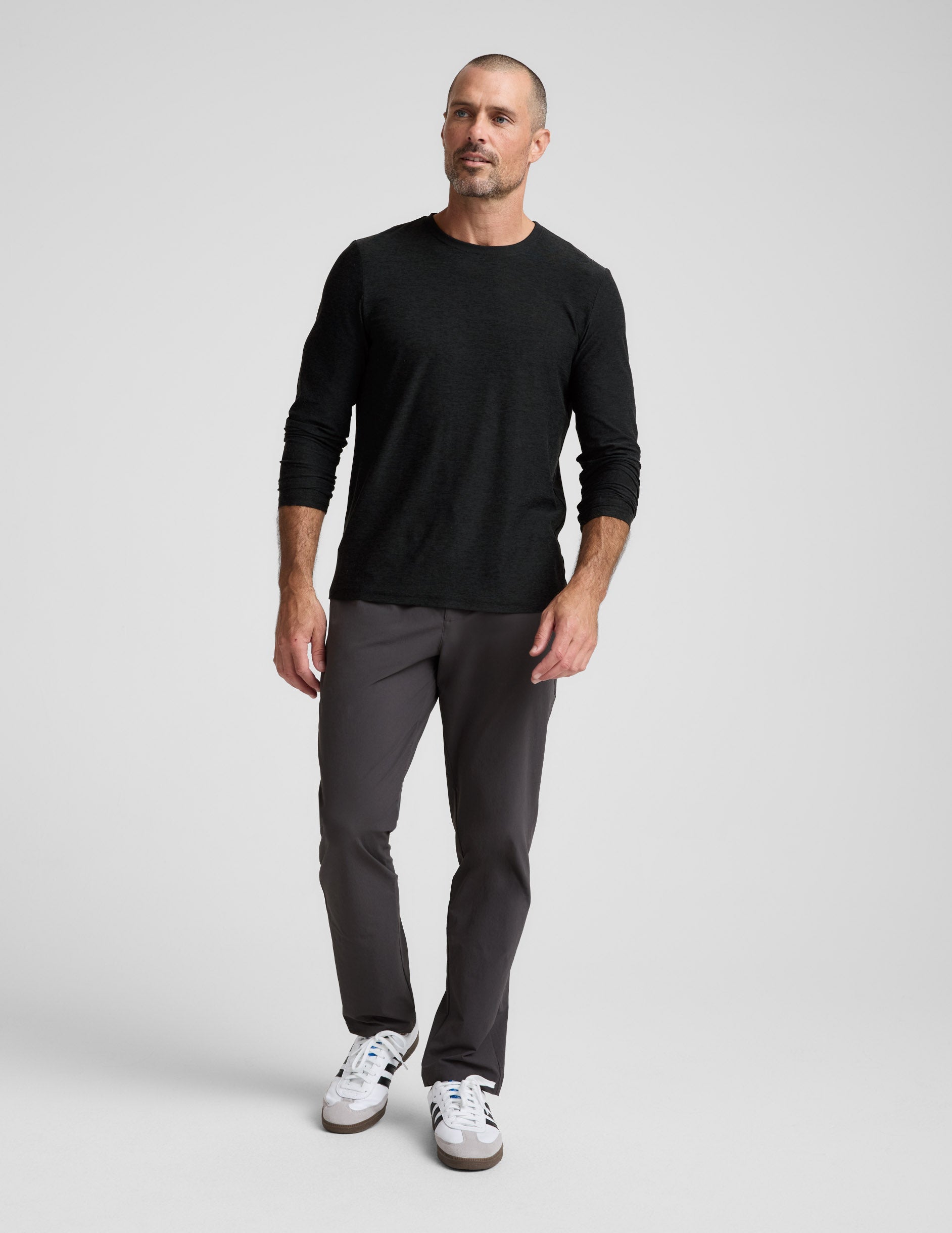 Man walking in dark charcoal Men's All Terrain Pant with a straight-leg fit, black long-sleeve shirt, and white sneakers.