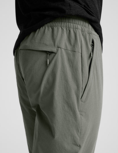 Side view of olive Men's All Terrain Pant showing gathered elastic waistband and side and back zipper pockets with pulls.