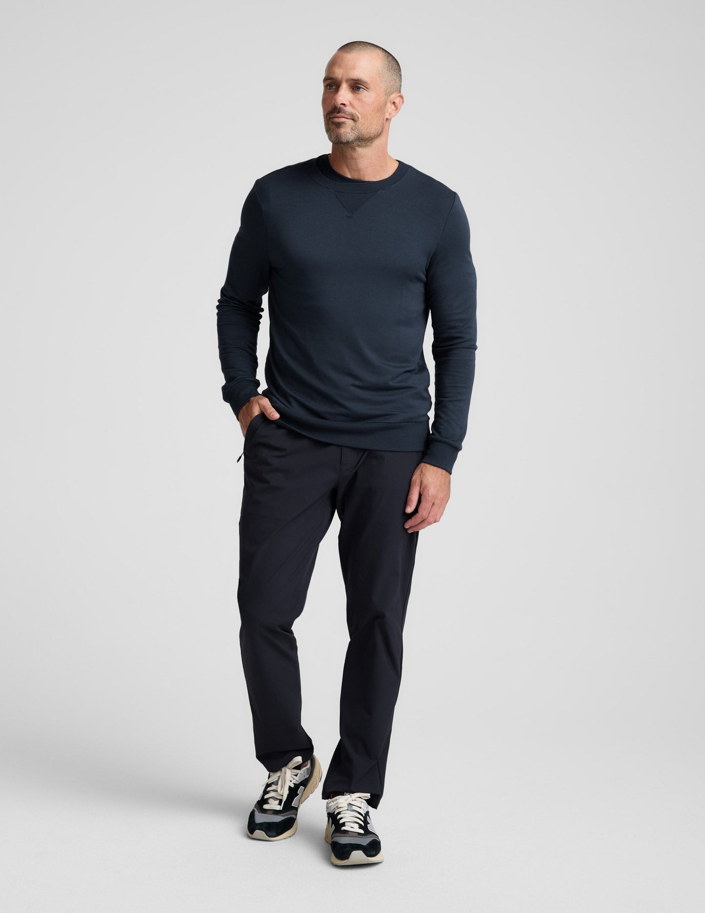 Man wearing navy Men's All Terrain Pant in a relaxed straight fit with zipper pockets, sweatshirt, and sneakers.