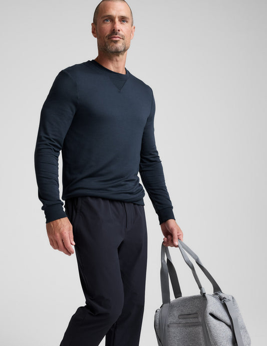Man wearing navy Men's All Terrain Pant with a relaxed fit and straight leg, holding a grey bag on a neutral background.