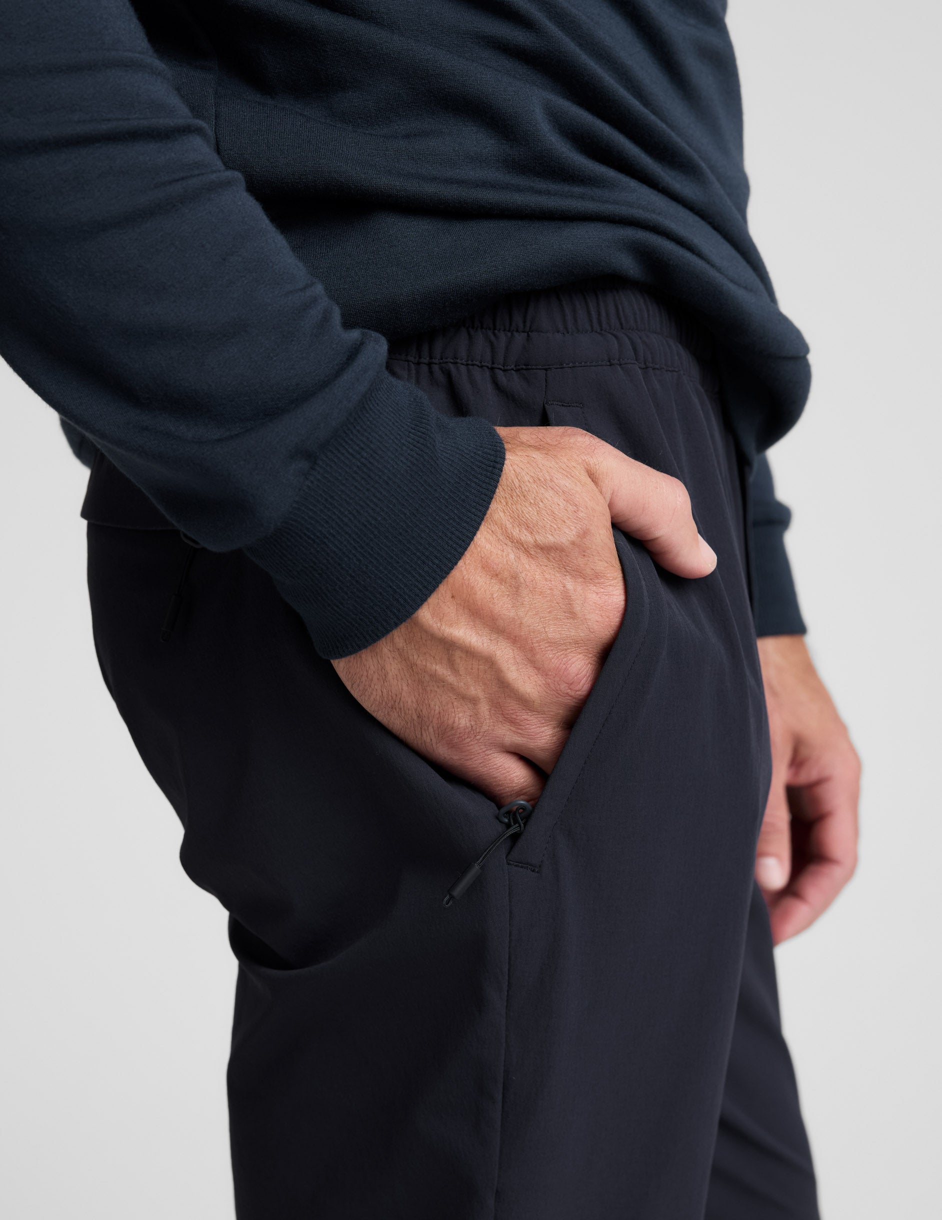 Close-up of navy Men's All Terrain Pant featuring an elastic waistband and a hand resting in a side zipper pocket.