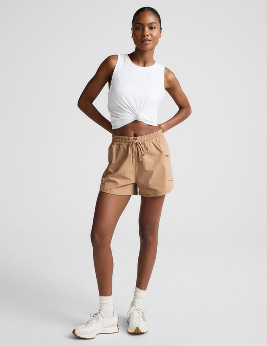 Woman wearing tan Peak™ 3" Short with a knotted white tank top, featuring a drawstring waist and side zip cargo pockets.