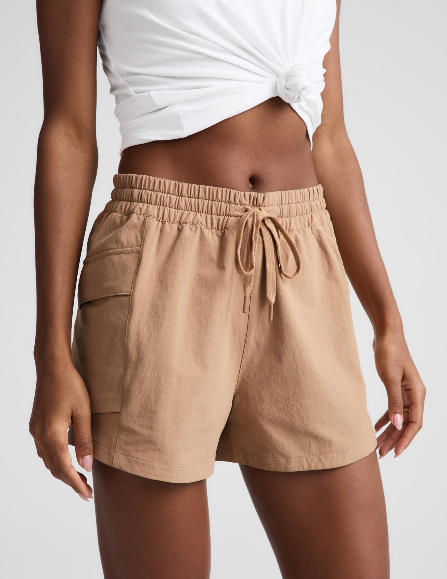 Woman wearing tan Peak 3" Short™ paired with a white knotted tank top, featuring an elastic waistband and drawcord.