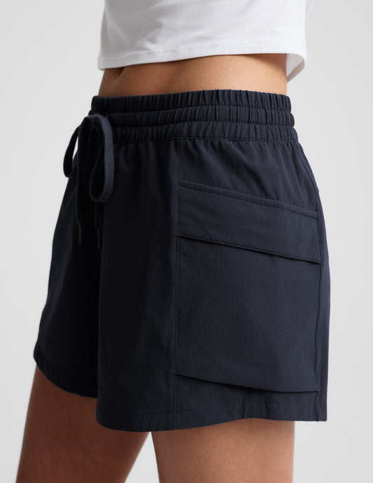 Woman wearing black Peak 3" Short with a white top. Side profile showing the gathered elastic waistband and cargo pocket.