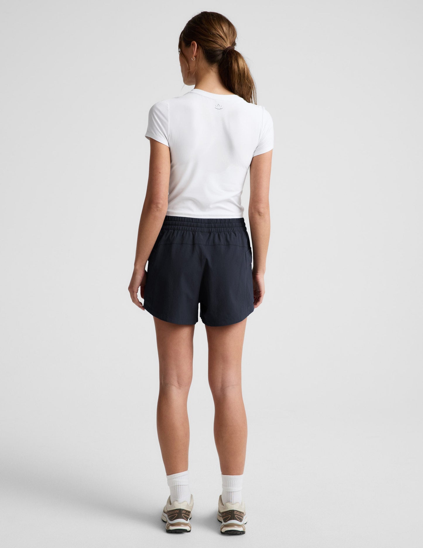 Rear view of woman wearing black Peak 3" Short™ with an elastic waistband, paired with a white t-shirt and sneakers.