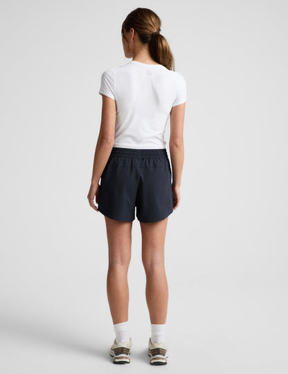 Rear view of woman wearing black Peak 3" Short™ with an elastic waistband, paired with a white t-shirt and sneakers.