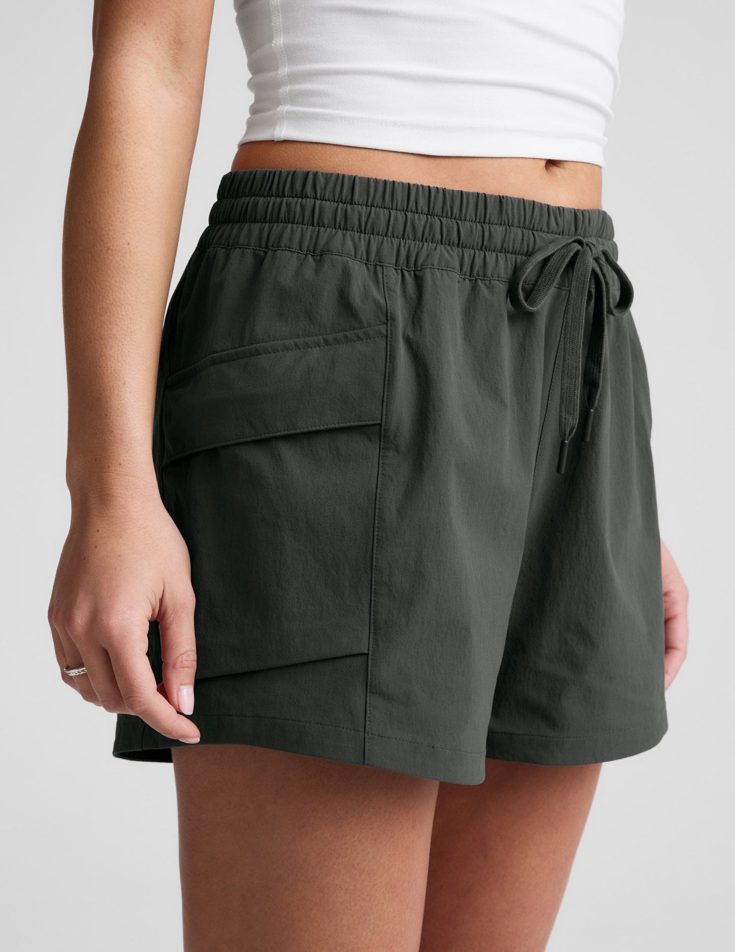Side profile of woman wearing Black Peak 3" Short™ with a white cropped tank top, showing the side patch cargo pocket.