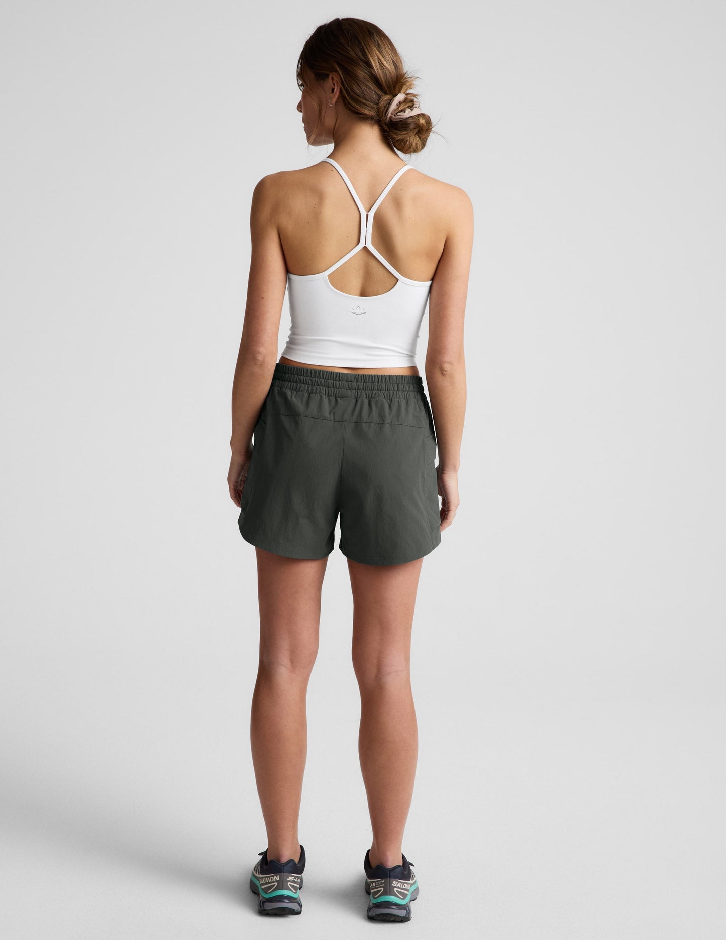 Rear view of woman wearing Dark Green Peak 3" Short™ paired with a white racerback crop top and sneakers.