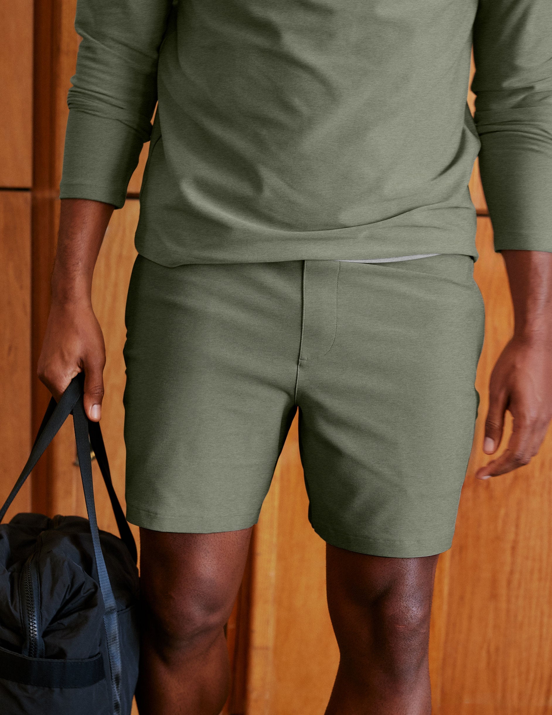 Man wearing Olive Spacedye™ Unlimited Men's Short paired with a matching long-sleeve top and holding a black bag.